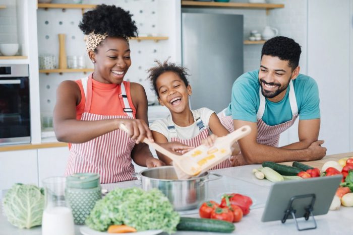 En glad familie laver mad sammen med friske grøntsager i et lyst køkken.